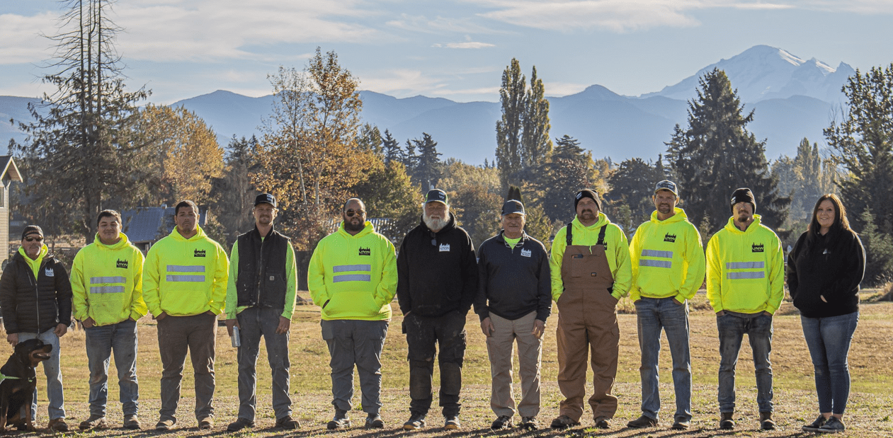 Group of workers standing outdoors with mountains and trees in the background.